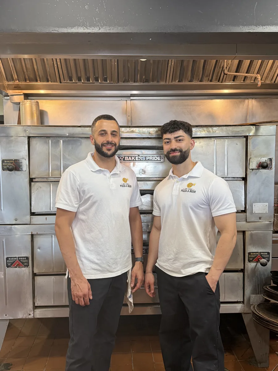 Co-owners Zee and Sadeer in Del Cerro Pizza & Beer polos, standing in front of the Bakers Pride ovens